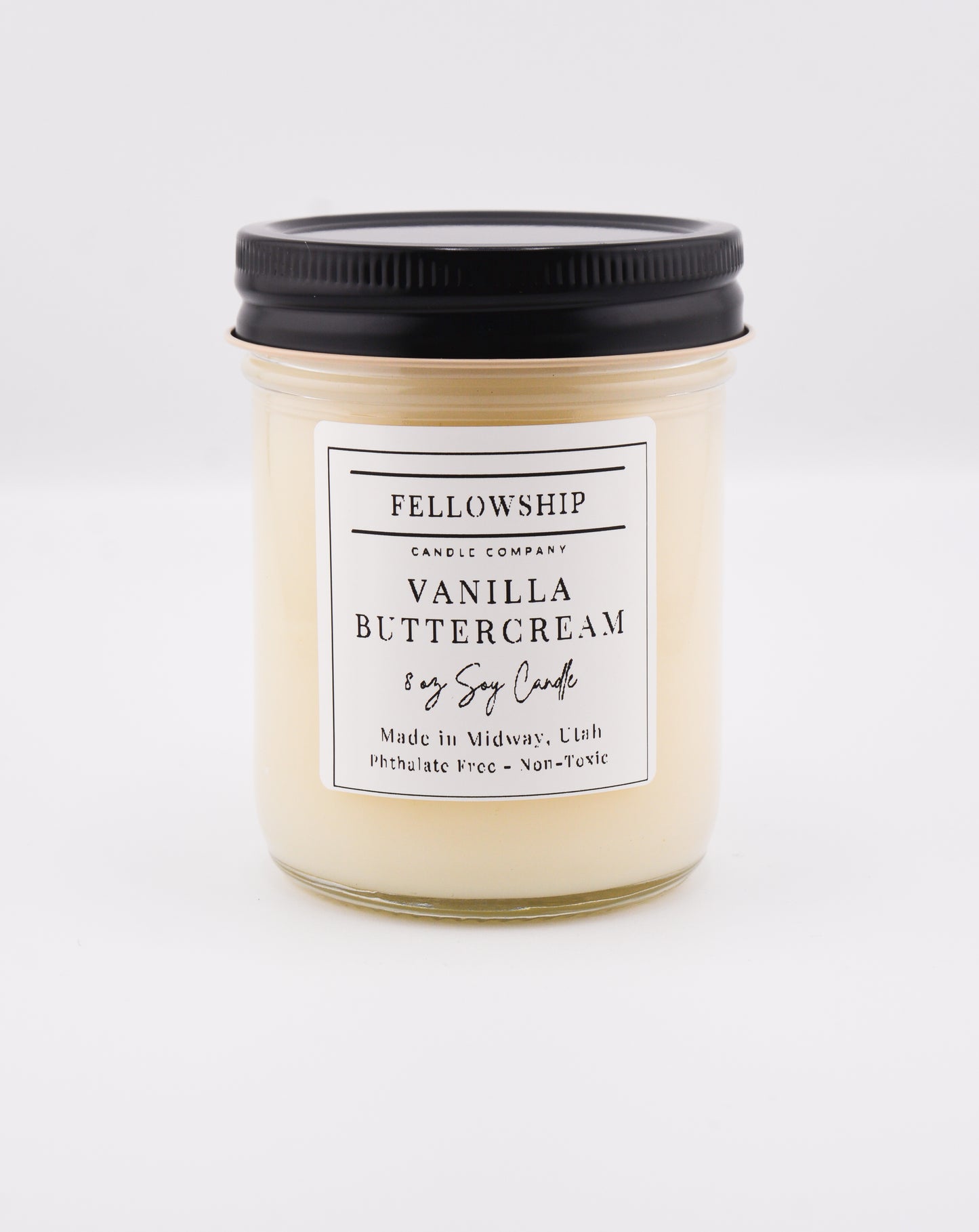 Vanilla buttercream candle with a black lid on a white background
