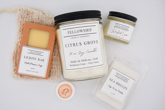 Collection of Fellowship Candle Company products including candles and a soap on a light background